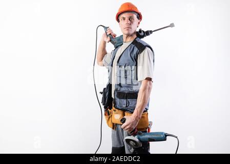 A builder with a hammer drill on his shoulder, and a angle grinder in his other hand, in a helmet, smiles. Stock Photo