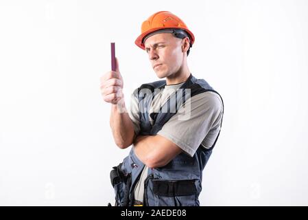 A builder in a helmet makes visual measurement with a marking pencil. Stock Photo