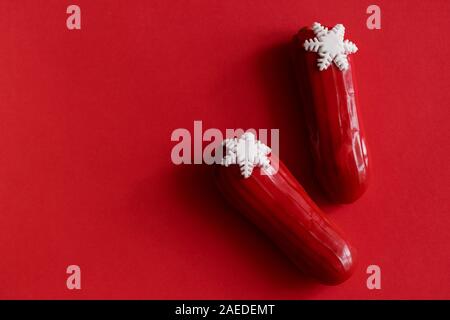 Red glazed eclair with white snowflakes in red colored background. Copyspace, flatlay, overhead, minimalism food photography concept. Christmas desser