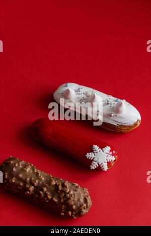 Red glazed eclair with white snowflakes on red colored background. Copyspace, flatlay, overhead, minimalism food photography concept. Christmas desser