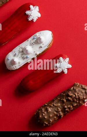 Red glazed eclair with white snowflakes on red colored background. Copyspace, flat lay, overhead, minimalist food photography concept. Christmas desse