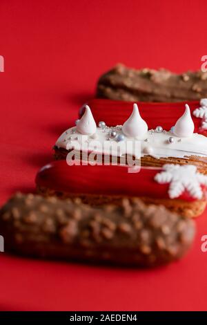 Red glazed eclair with white snowflakes on red colored background. Copyspace, close up, minimalist food photography concept. Christmas dessert