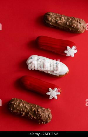 Red glazed eclair with white snowflakes on red colored background. Flatlay, overhead, minimalist food photography concept. Christmas dessert