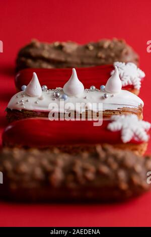 Red glazed eclair with white snowflakes on red colored background. Close up, minimalist food photography concept. Christmas dessert
