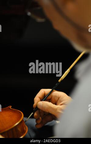 Master luthier violin maker varnishing a hand made violin stringed lute as final touches to finish his creation in his workshop in Cremona, Lombardy Stock Photo