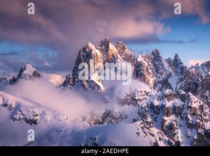 Snowy mountain peaks in fog and blue sky with clouds at sunset Stock Photo