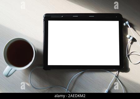 A blank tablet, earphones and a cup of tea on the wooden table. Business and education background. Flat lay, copy space, view from above. Stock Photo