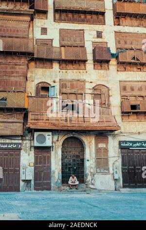 Arabic senior sitting on the steps in front of the door of a coral town house in the historic district Al Balad in Jeddah, KSA, Saudi Arabia Stock Photo