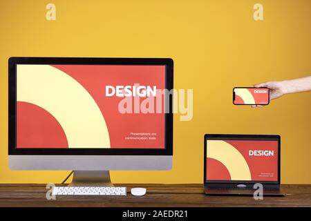 Web design concept with hand holding smartphone, computer and laptop at wooden table over pop yellow background, copy space Stock Photo