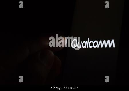 Qualcomm logo on a glowing screen and a hand pointing at it. Stock Photo