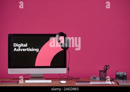 Digital advertising concept with computer and office supplies at wooden table over purple background, copy space Stock Photo