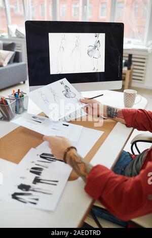Side view closeup of tattooed male hands holding fashion sketches over workplace in atelier or design studio, copy space Stock Photo