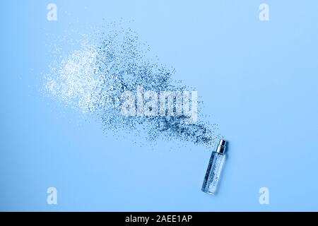 Stylish bottle of perfume with spray of sparkles on trendy blue background. Luxury perfume concept. Creative trendy flat lay with space for text. Stock Photo