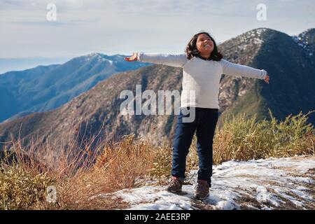 A little girl on the edge of a snow covered mountain, expressing joy after reaching the hiking trails summit in San Bernardino mountains. Stock Photo