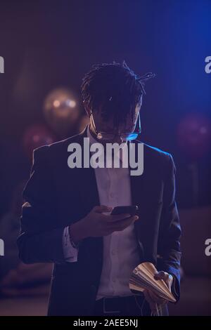 Waist up portrait of elegant African-American man checking smartphone messages in dimly lit room at night club, copy space Stock Photo