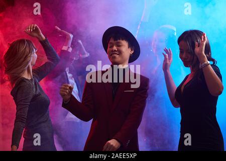 Waist up portrait of trendy Asian man dancing in smoky nightclub surrounded by beautiful women, copy space Stock Photo