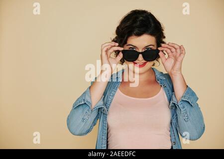 Cheerful smiling woman in denim shirt putting on sunglasses and looking at camera Stock Photo