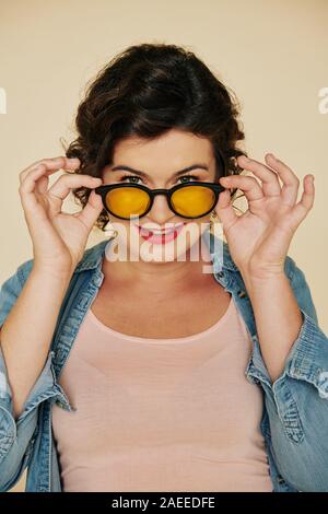 Portrait of smiling pretty woman putting on glasses with yellow lens Stock Photo