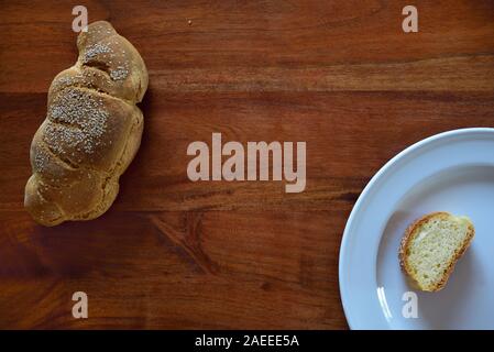 A traditional handmade fresh bread with sesame lies on a wooden table from above and beside it, on a white plate, a slice of bread with space in the m Stock Photo