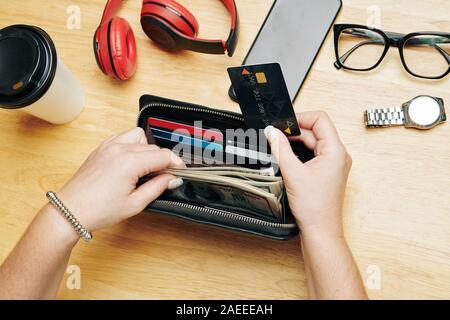 Hands of female shopaholic taking stack of money and credit card out of purse Stock Photo