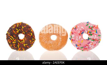 Three cake donuts in a row with reflection on table in front of them. Chocolate, sugar sprinkles, strawberry with candy sprinkles. Stock Photo