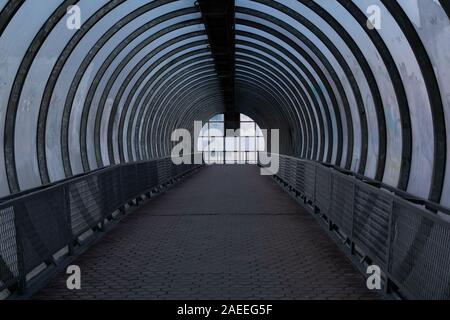 A long pedestrian tunnel with metal arches and glass design. Aerial pedestrian crossing over the highway, perspective goes to the horizon, a dark empt Stock Photo