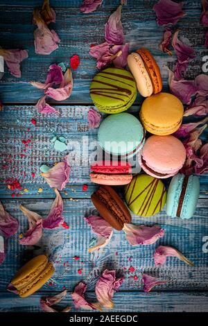 Great Photo of Assorted and Colorful  Macaroons Arranged Beautifully on top of Blue Wooden Table decorated with purple flower petals Stock Photo