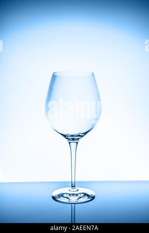 Red wine glass on the light background. Fine cristal glassware concept. Vertical, toned in blue Stock Photo