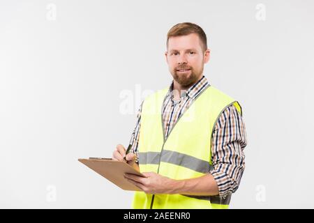 Happy young bearded engineer with clipboard and pen making working notes Stock Photo