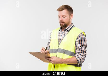 Young bearded engineer with clipboard and pen making working notes in isolation Stock Photo