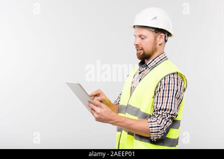Young engineer or foreman in workwear pointing at display of digital tablet Stock Photo