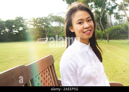 Portrait of young student smiling sitting at outdoor under sunlight on greenfield in the university Stock Photo