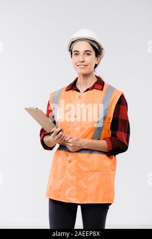 Successful female engineer in helmet and orange jacket holding clipboard Stock Photo
