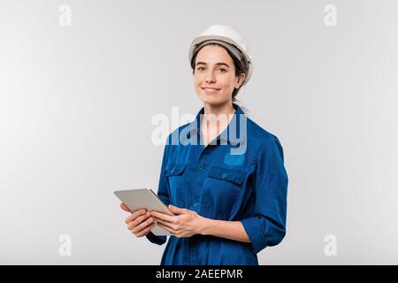 Smiling successful female engineer in workwear and hardhat using touchpad Stock Photo
