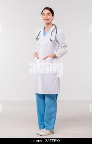 Pretty young brunette clinician in medical uniform keeping her hands in pockets Stock Photo