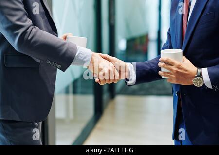 Cropped image of business people with coffee cups shaking hands and greeting each other in office corridor Stock Photo