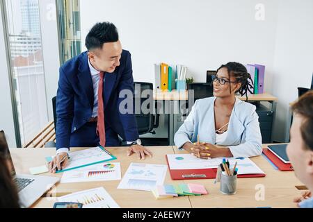 Positive coworkers meeting in office and discussing charts and graphs with sales data Stock Photo