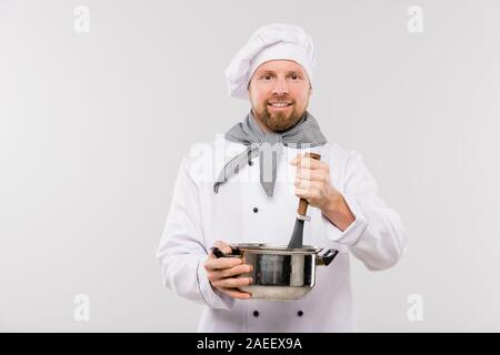 Professional male chef mixing soup or other meal in pan while cooking food Stock Photo