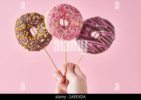 Three donuts in woman hand on pink background. Creative food minimalism style Stock Photo