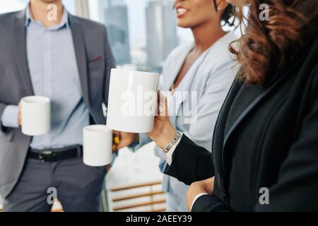 Businesswoman with big mug of coffee talking and gossiping with her coworkers during break Stock Photo