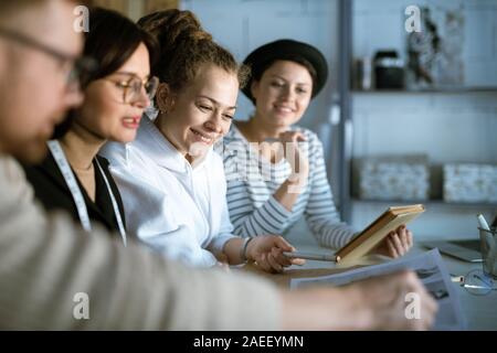 Young creative fashion designers discussing sketches while gathered in studio Stock Photo