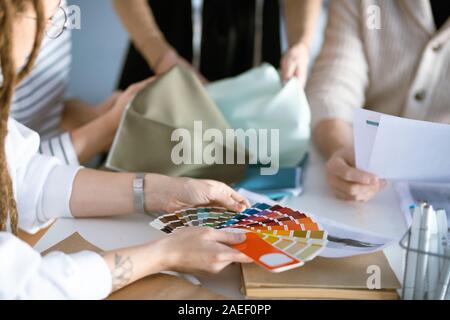 Hands of designer holding color palette over desk while working with colleagues Stock Photo