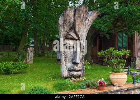 Wooden sculpture with man's face is standing near green trees in the park. Stock Photo