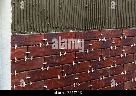 Close-up view of the outdoor wall with brown tiles. The man lays out the tile on this wall. Stock Photo