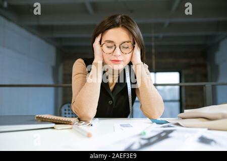 Young concentrated or tired female designer touching head during work in studio Stock Photo