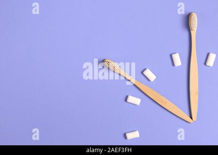 Dental care. Two wooden bamboo eco friendly toothbrushes and chewing gum in the form of hours on a purple background. Eco friendly and reuse concept. Stock Photo