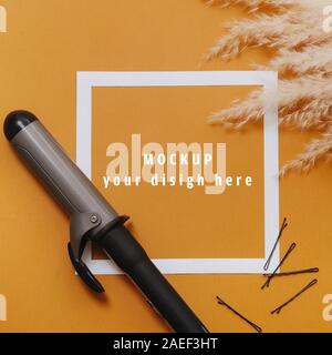 Hairdresser tools: curling iron and bobby pins over orange. Top view Stock Photo