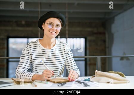 Young creative designer sitting by desk in studio and drawing fashion sketch Stock Photo