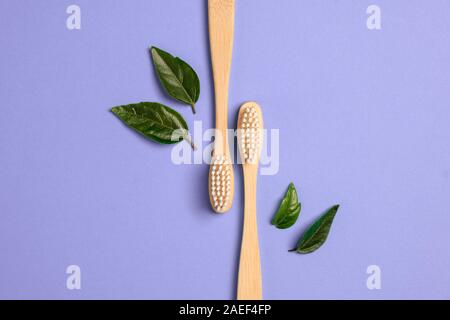 Two wooden bamboo eco friendly toothbrushes and green leaf on purple background. Dental care and zero waste concept. Flat lay, top view, copy space Stock Photo