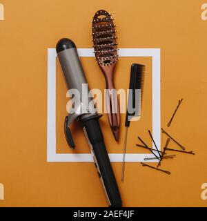 Barber tools: curling iron, hairbrush, rat tail comb, bobby pins over orange Stock Photo